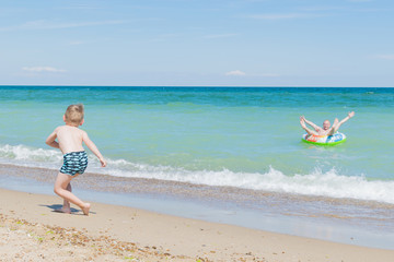 Obraz premium A little boy with his dad is resting on the sea. Dad swims in an inflatable circle on the water, the son runs along the shore.