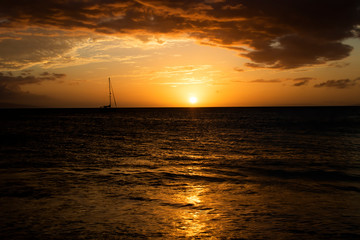 Sunset seascape with boat on horizon under orange sky