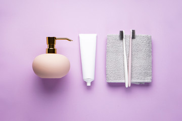 Toothbrushes on a towel and cream dispenser on a pink background. Flat lay