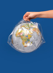 Hand holding a world globe wrapped in plastic.