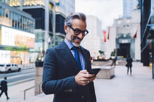 Smiling trendy businessman with smartphone in megapolis street