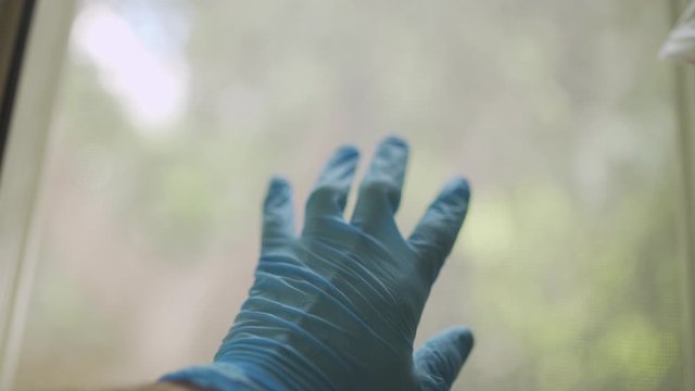 Hand wearing latex protection glove touches a window indoors in apartment