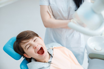 Fototapeta na wymiar Patient in dental chair. Teen boy having dental treatment at dentist's office. Healthy teeth, dental care concept.