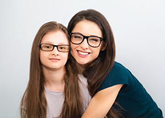 Young casual toothy smiling mother and happy kid in glasses hugging on light blue background. Closeup studio portrait. Teaching kids staying at home. Online education.