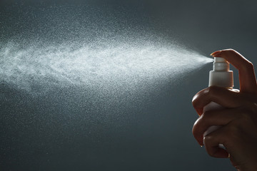 Close-up view of human hand and antiseptic spray bottle on dark background. Control Epidemic Prevention measures of coronavirus. - obrazy, fototapety, plakaty