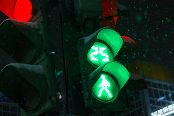 Green light traffic light on dark background with walking pedestrian at night during snowfall in...
