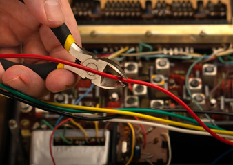 Hand with wire cutters cuts the red wire coming from the electronic device