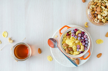 top view of healthy nutritious breakfast for children and adults on wooden background, copy space. corn flakes with honey, berries, cranberries, nuts, cashews, almonds.