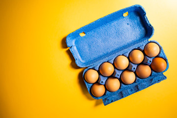 Fresh eggs in blue carton box isolated on yellow background