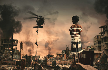 Homeless little boy watching roping soldier in destroyed and bombarded city between smoke.
