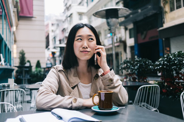 Pleased Asian woman talking on smartphone in cafe
