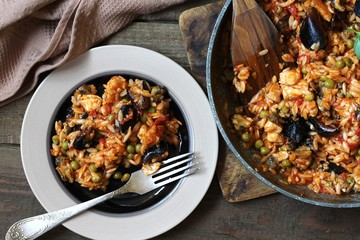 orzo pasta with mussels, seashells and chicken. Seafood paella, traditional spanish dish. Paella on rustic black wooden table. Top view
