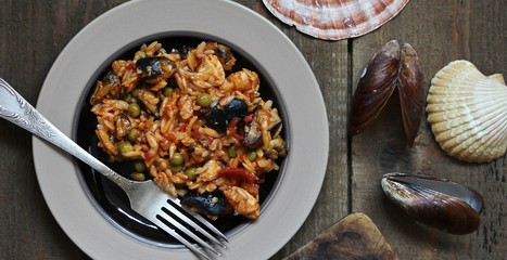 orzo pasta with mussels, seashells and chicken. Seafood paella, traditional spanish dish. Paella on rustic black wooden table. Top view