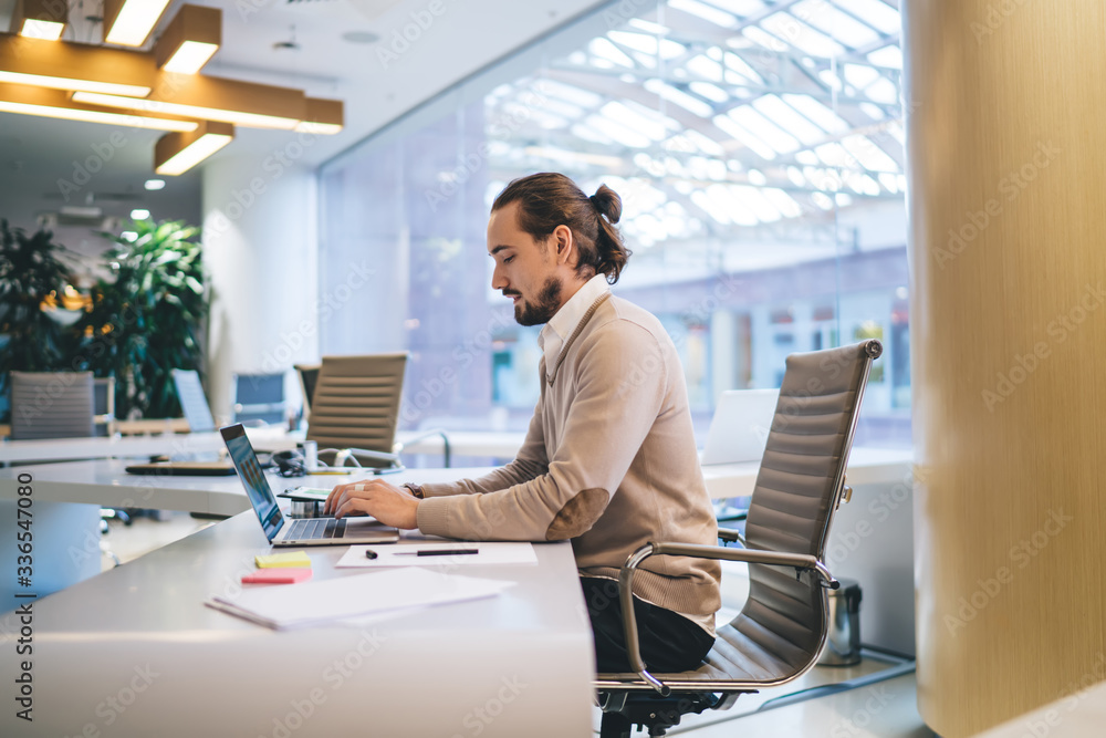 Poster caucasian freelancer working in modern coworking space using high speed internet connection on lapto