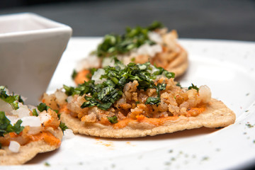 Chalupas con chicharrón de camarón, salsa picante, cilantro y cebolla, comida mexicana, plato blanco sobre fondo negro	