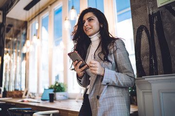 Smiling lady surfing cellphone in cafe