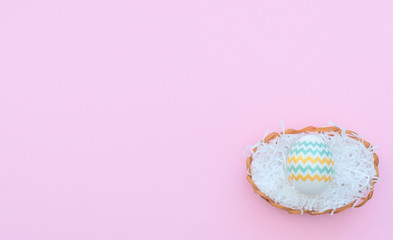 Decorated Easter egg lies in the basket on pink background. Happy Easter holiday concept. Greeting, invitation card. Flat lay style with copy space.