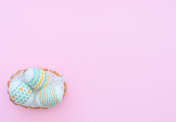Decorated Easter eggs lie in the basket on pink background. Happy Easter holiday concept. Greeting, invitation card. Flat lay style with copy space.