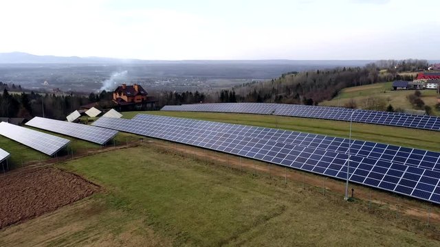 Aerial view of large field of solar photo voltaic panels system producing renewable clean energy on green grass background.
