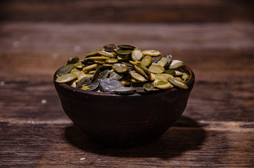 Peeled pumpkin seeds in a ceramic bowl on a wooden kitchen table.