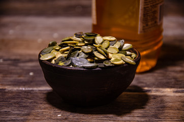 Peeled pumpkin seeds in a ceramic bowl on a background of a bottle of pumpkin oil on a wooden table.