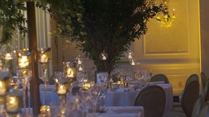 Round wedding table with green branches in the middle, ceremonial table serving and chiavari chairs, burning candles and festive decorative elements