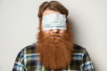 A man with a red hair and a red beard wearing a face mask over his eyes.  A bearded man with a...