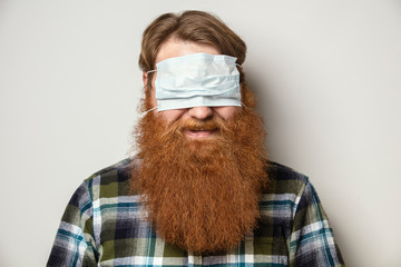 A man with a red hair and a red beard wearing a face mask over his eyes.  A bearded man with a...