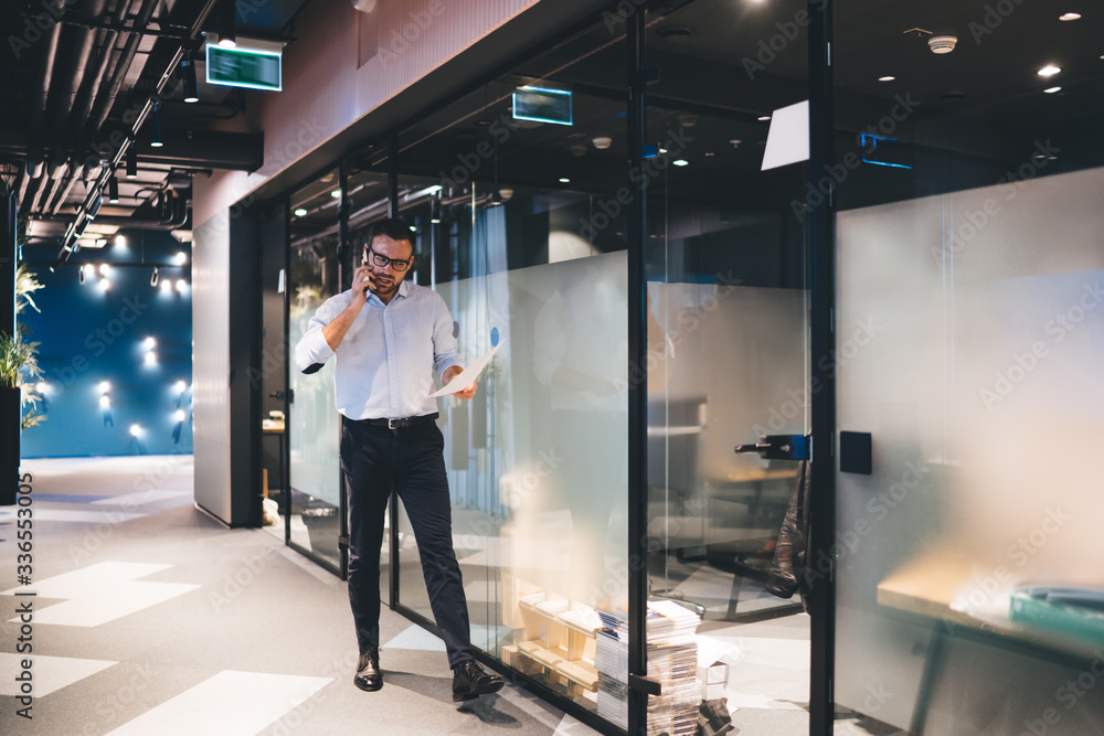 Poster financial marketer holding paper documents in hand and making cellphone conversation with executive 