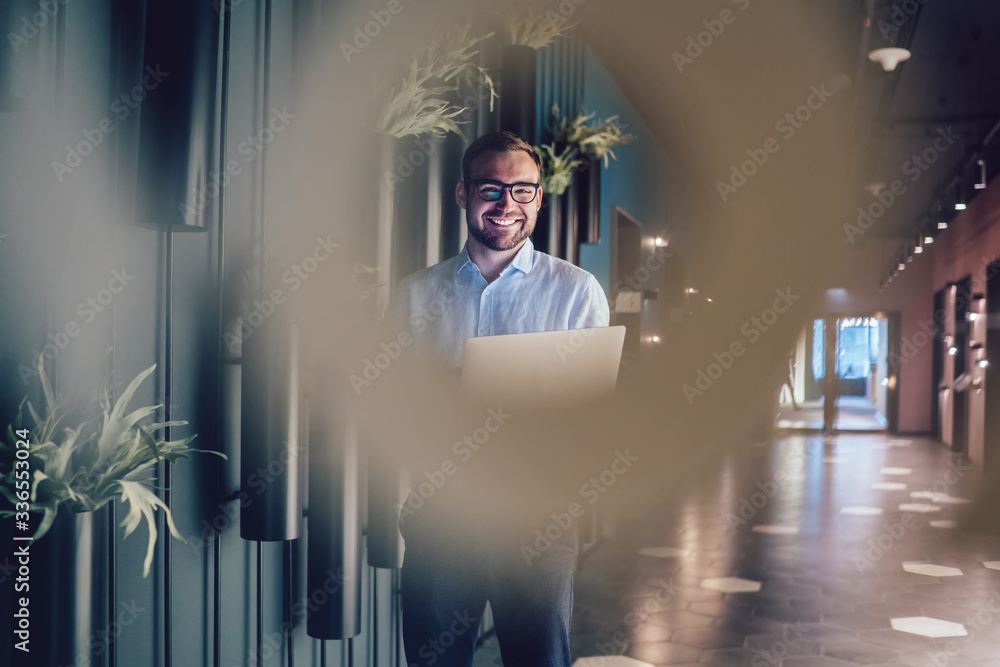 Poster cheerful male executive manager in optical glasses holding laptop computer in hands and laughing dur
