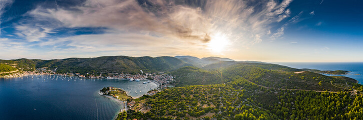 Fototapeta na wymiar Aerial view of marina Vis at sunset, Croatia, a lot of chaotically standing boats in a bay, roofs of orange color, sunshine, hills with green trees, ferry station