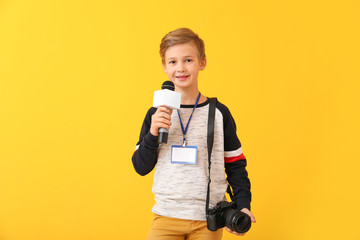 Little journalist with microphone and camera on color background