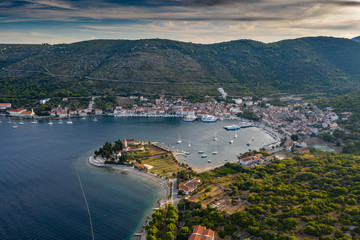 Naklejka na ściany i meble Aerial view of marina Vis at sunset, Croatia, a lot of chaotically standing boats in a bay, roofs of orange color, sunshine, hills with green trees, ferry station