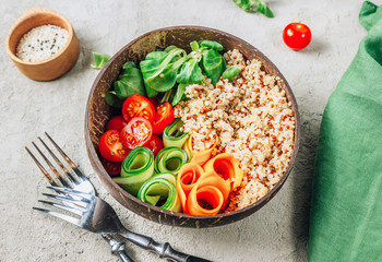 Vegan Buddha bowl. Healthy meal quinoa, tomato, cucumber, carrot, radish, corn salad in coconut bowls on concrete background.