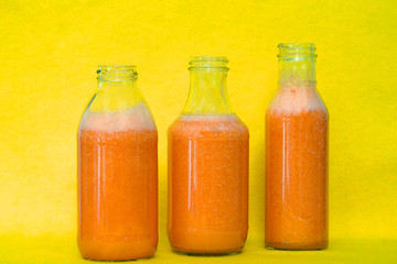 Glass bottles filled with colorful fresh homemade orange, carrot and ginger smoothies