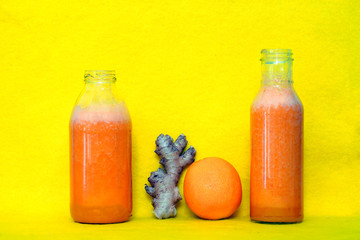 Glass bottles filled with colorful fresh homemade orange, carrot and ginger smoothies