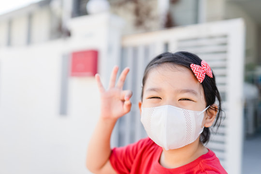 Covid-19 Coronavirus Pandemic Concept.Little Chinese Girl Wearing Mask For Protect Virus And OK Finger Hands Gesture For Stop Covid19 Virus Outbreak.Stay Strong At Home Coronavirus Virus Symptoms.