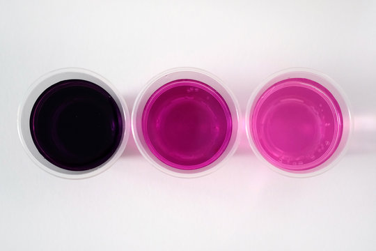 Potassium permanganate on a white background. Black powder potassium permanganate in a plastic glass with water. A solution of potassium permanganate in water different fortress