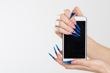 Woman hands with stiletto nails holding phone. Art Manicure. Modern style blue Nail Polish. Beauty hands holding mobile cellphone. Stylish Colorful stiletto Nails isolated white background