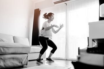 Video streaming Stay home.home fitness workout class live streaming online.Asian woman doing strength training cardio aerobic dance exercises watching videos in the living room at home.Covid-19.