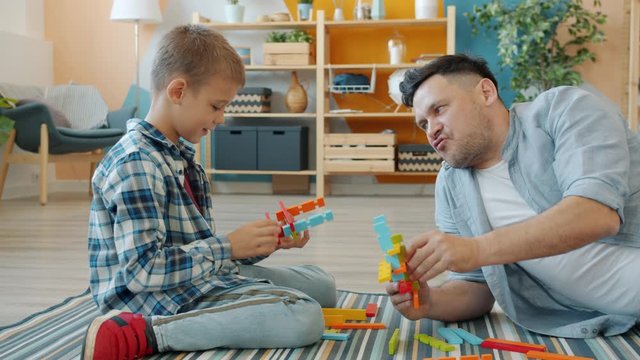 Happy kid is playing with joyful dad using construction blocks enjoying funny game at home on floor having fun and talking. Childhood and people concept.