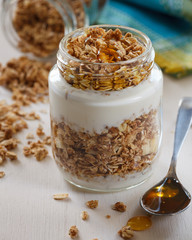 Pote de iogurte e granola com mel sobre mesa branca