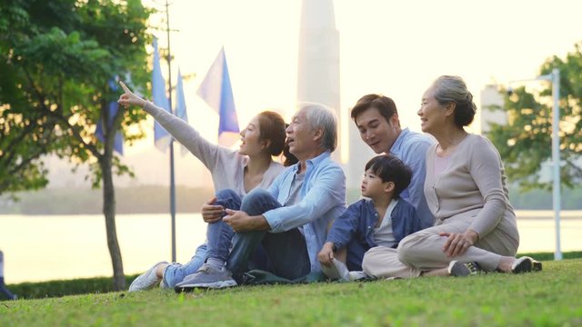 happy three generational family relaxing sitting on grass in city park