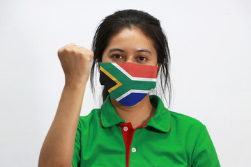 South Africa flag on hygienic mask. Masked woman prevent germs and wear green shirt. Tiny Particle or virus corona or Covid-19 protection. Lift the fist up for meaning fighting.