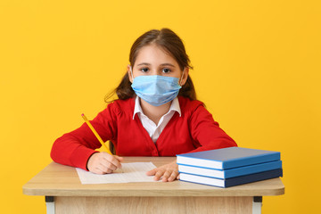 Pupil in medical mask passing exam against color background. Concept of epidemic