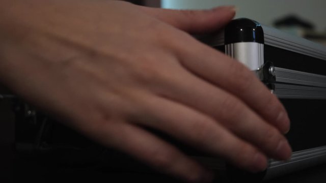 Close up of female hands opening silver metal suitcase with locking system. Concept. Opening aluminum carrying case to find shining mysterious object inside.