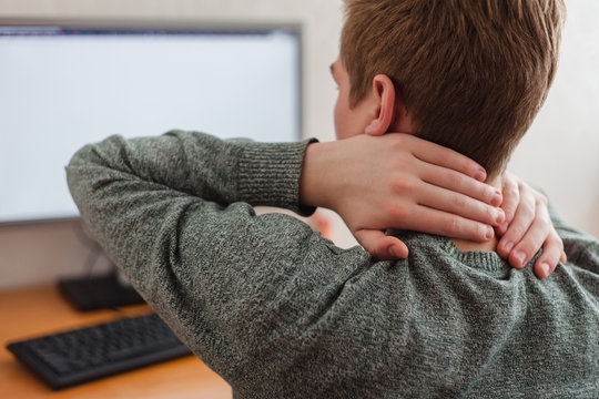 Tired man after working at the computer massages rubs his neck, chronic pain in the neck and back, discomfort after long sedentary work in incorrect posture, fibromyalgia concept and acute chondrosis.