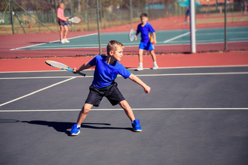 Beautiful young boy on the tennis court, standing in a wide stance waiting for the return tennis...