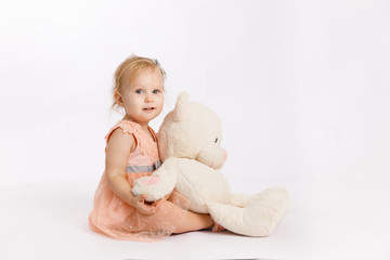Little cute girl holds a large Teddy bear enjoy festive birthday event wear pink pastel summer dress isolated on a white background. Birthday present.