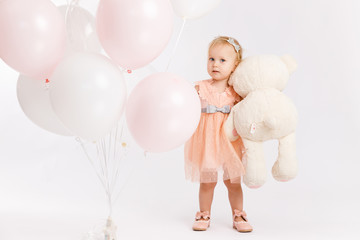 Little cute girl holds branch of balloons and large Teddy bear enjoy festive birthday event wear pink pastel summer dress isolated on a white background.